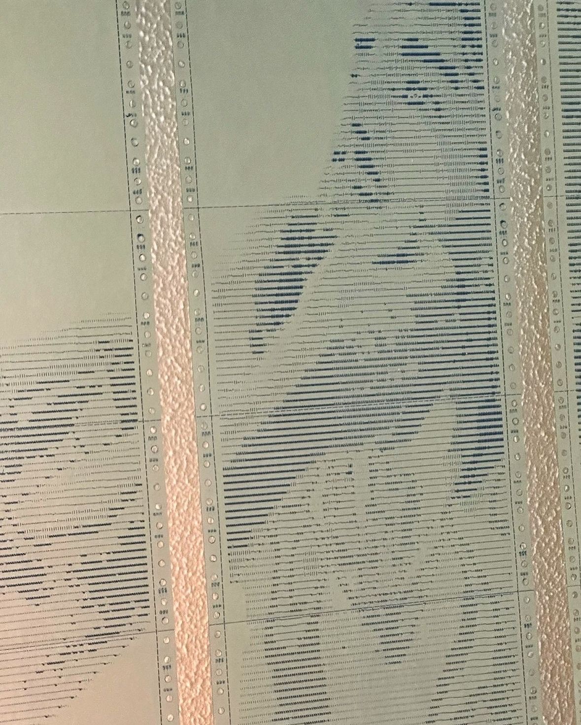 Backlit detail of AWAITING INPUT by CHARACTERS — dot-matrix paper held to light showing paper texture, perforated edges, and ASCII character rendering of a reclined nude figure. 2024.